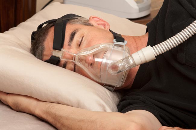 Man sleeping in bed with help from a CPAP sleep apnea machine.