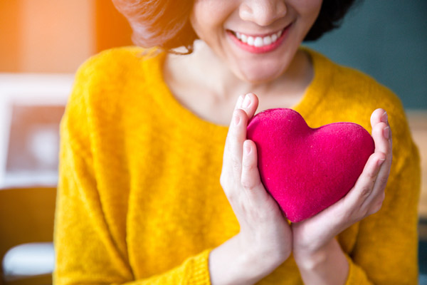 A woman smiling and holding a felt heart.