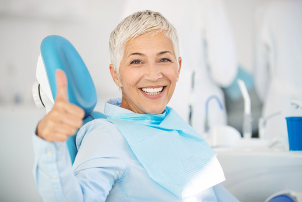 Mature woman smiling in a dental chair showing a thumbs up