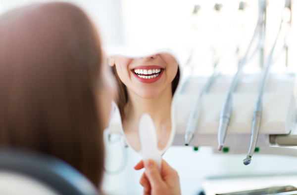 Woman looking at her smile in a mirror, at Fusion Dental Specialists in Happy Valley, OR.