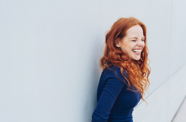 Woman leaning against the wall and smiling, at Fusion Dental Specialists in Happy Valley, OR.